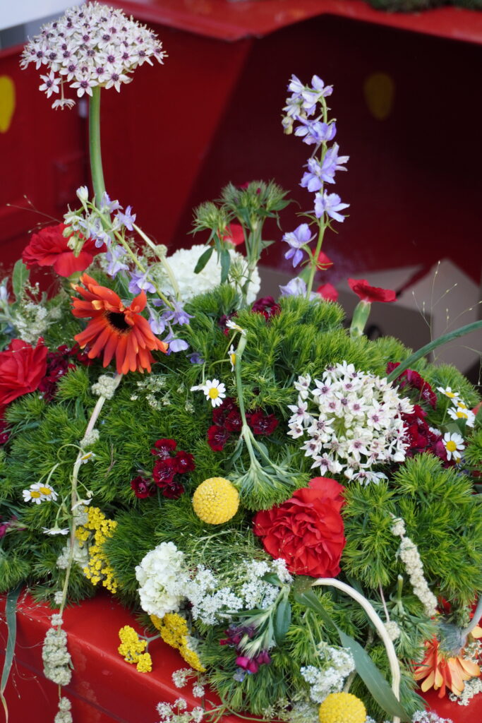Nahaufnahme eines farbenfrohen Blumenarrangements mit roten, gelben, weißen und violetten Blüten auf einem roten Hintergrund.