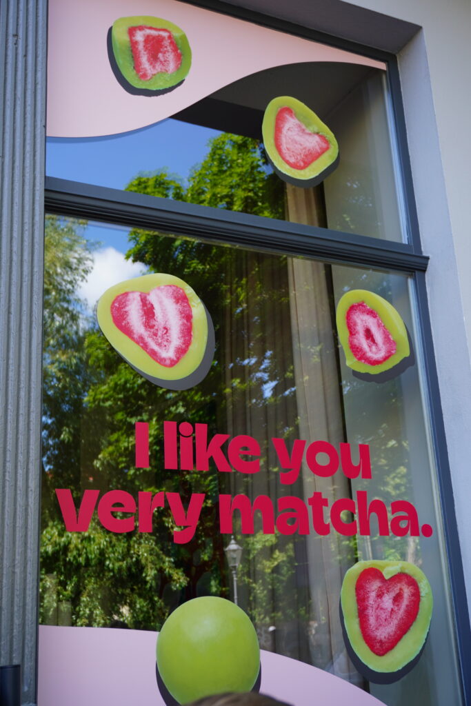 Schaufenster mit dem Slogan „I like you very matcha“ und dekorativen Aufklebern in Herzform mit Matcha-Erdbeer-Motiv.
