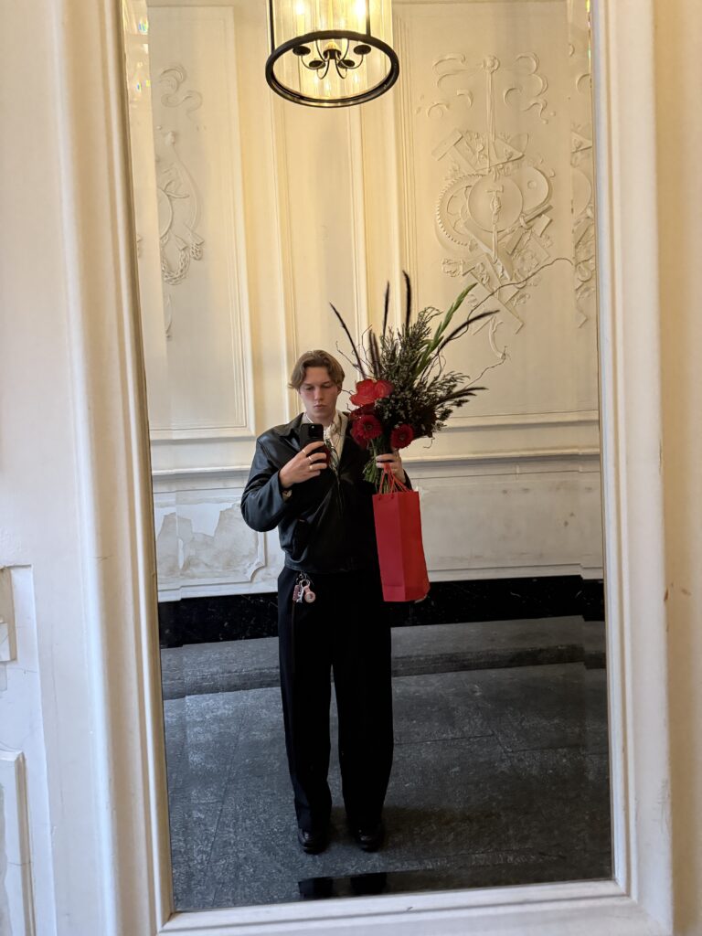 Spiegel-Selfie mit floraler Mission – schwarze Lederjacke, rote Tüte, und ein Bouquet wie ein Kunstwerk.