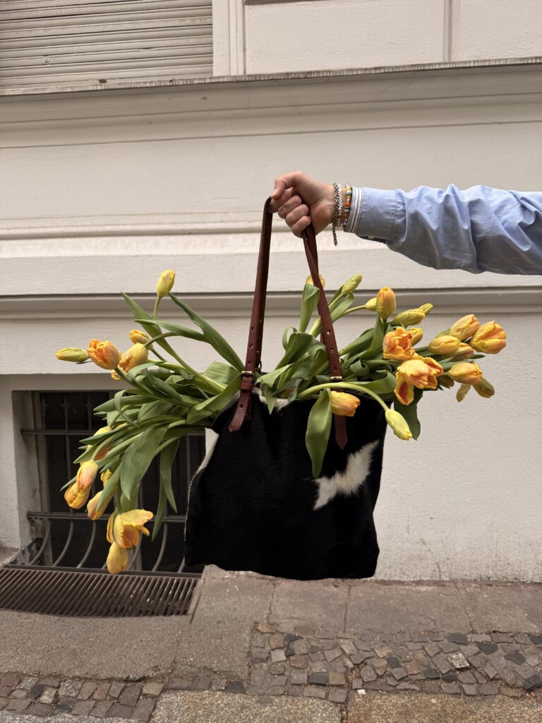 Junge Person mit hellblauem Hemd hält eine Tasche mit einem großen Strauß gelber Tulpen.